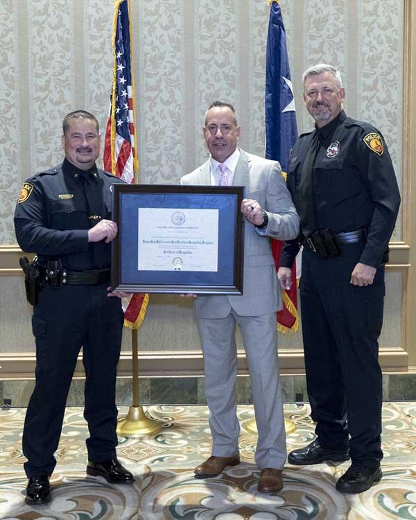Two police officers and a gentleman holding a framed award.