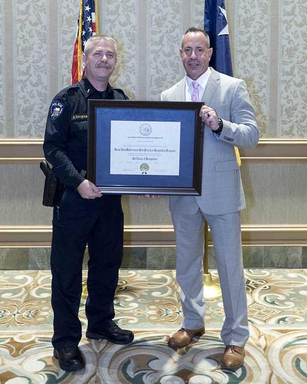 A police officer and a gentleman holding a large, framed award.