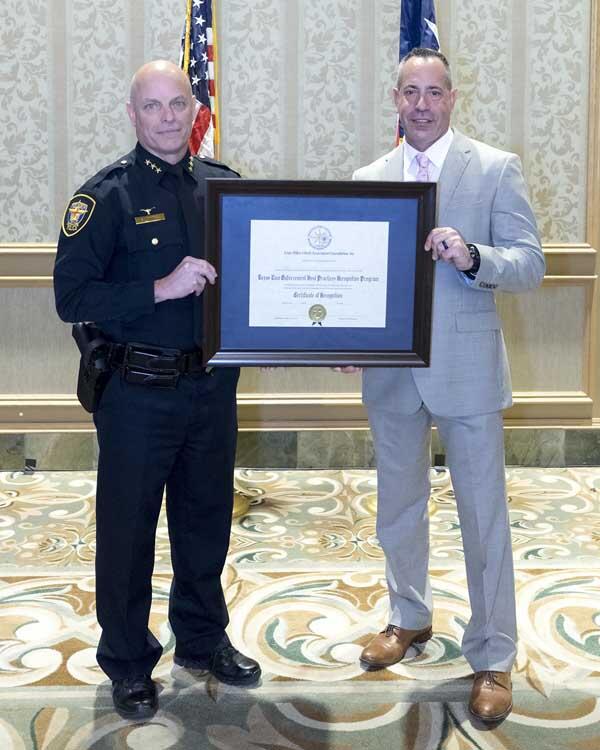 A police officer and gentleman stand on either side of a framed award.