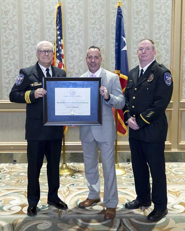 15.	A gentleman stands between two police officers holding a large, framed award.