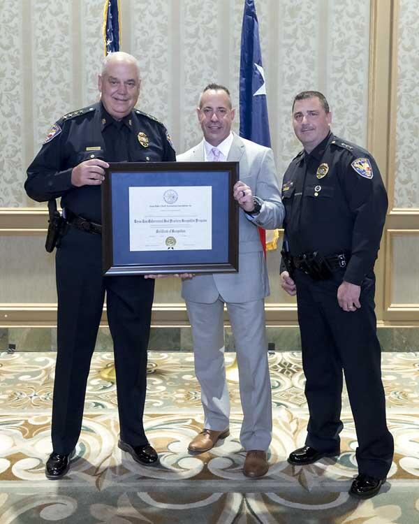 Two smiling police officers stand with a gentleman and hold a large, framed award.