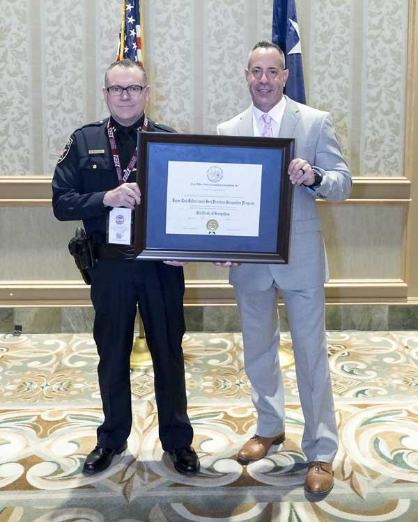 A police officer stands with a gentleman as the hold a large, framed award. 