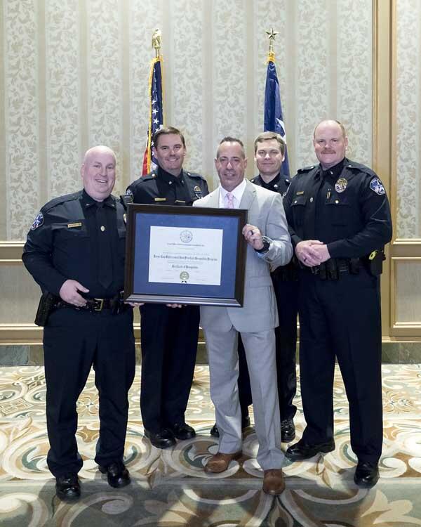 Four police officers and a gentleman stand together holding a large, framed award.