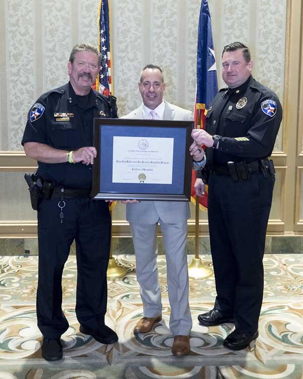 Two police officers stand with a gentleman holding a large, framed award.