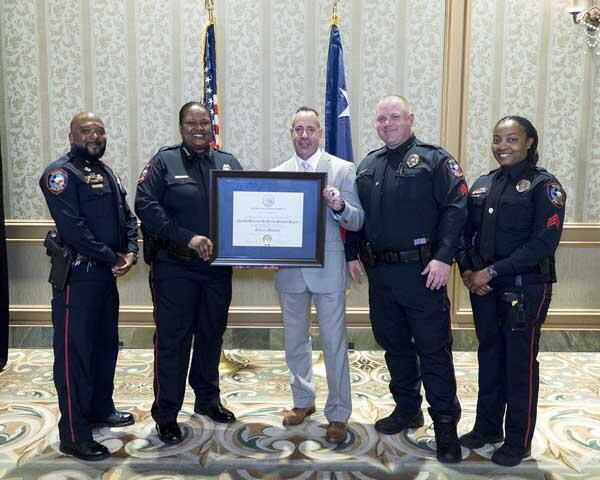 Four police officers stand along either side of a gentleman holding a large, framed award.