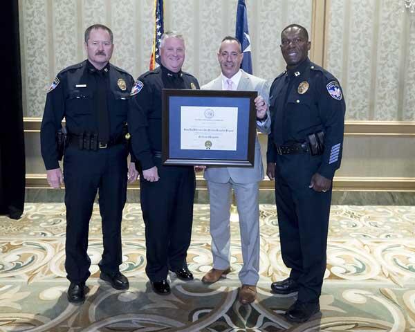 Three police officers and a gentleman stand together smiling as they hold a large, framed award.