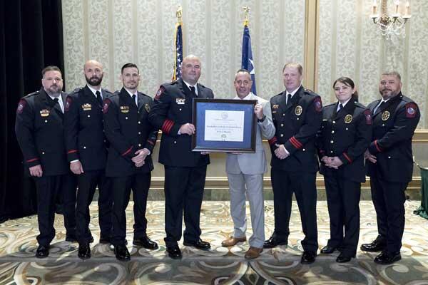 A group of seven police officers stand along side a gentleman and smile as he holds a large, framed award.