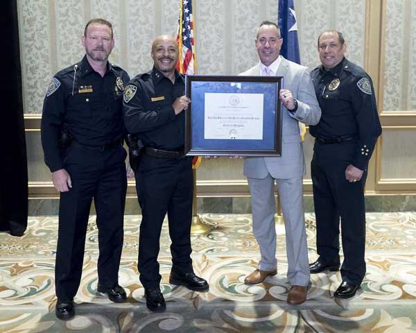 Three police officers stand with a gentleman holding an award.