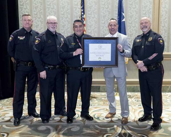 A gentleman stands with four police officers as they hold a large, framed award. 