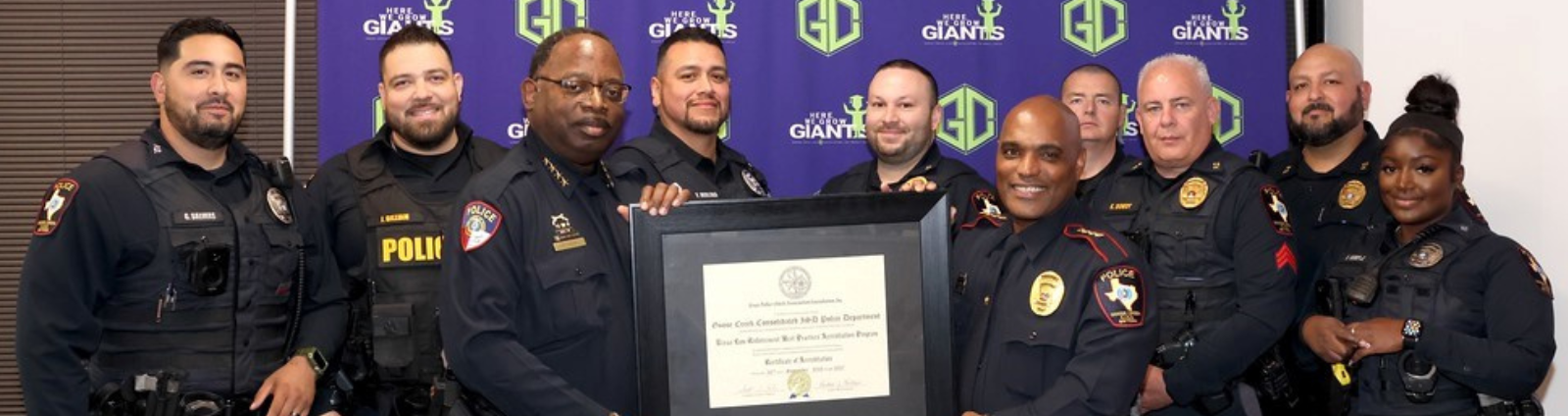 10 uniformed officers holding a plaque standing in front of a multicolored banner